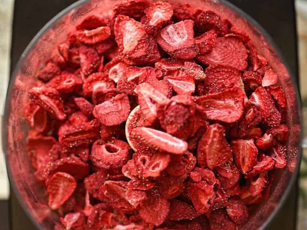 A close-up of a bowl filled with freeze-dried strawberry slices. The strawberries are vibrant red with visible seeds and varied textures, suggesting a crunchy texture.